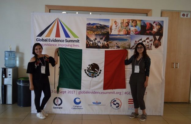 Cindy and Itzel standing next to the Global Evidence Summit poster