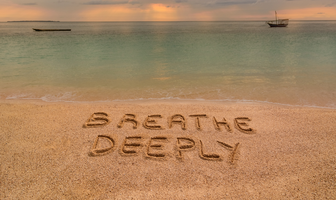 In the photo a beach in Zanzibar at sunset where there is an inscription on the sand "Breathe Deeeply".