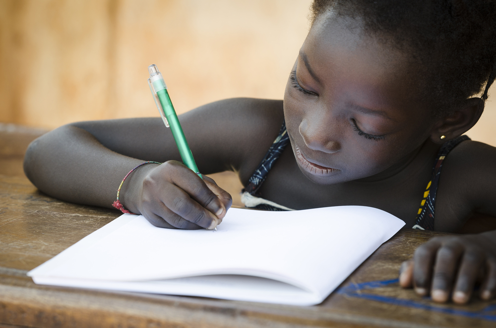 Young african girl writing in a workbook - to symbolise schooling